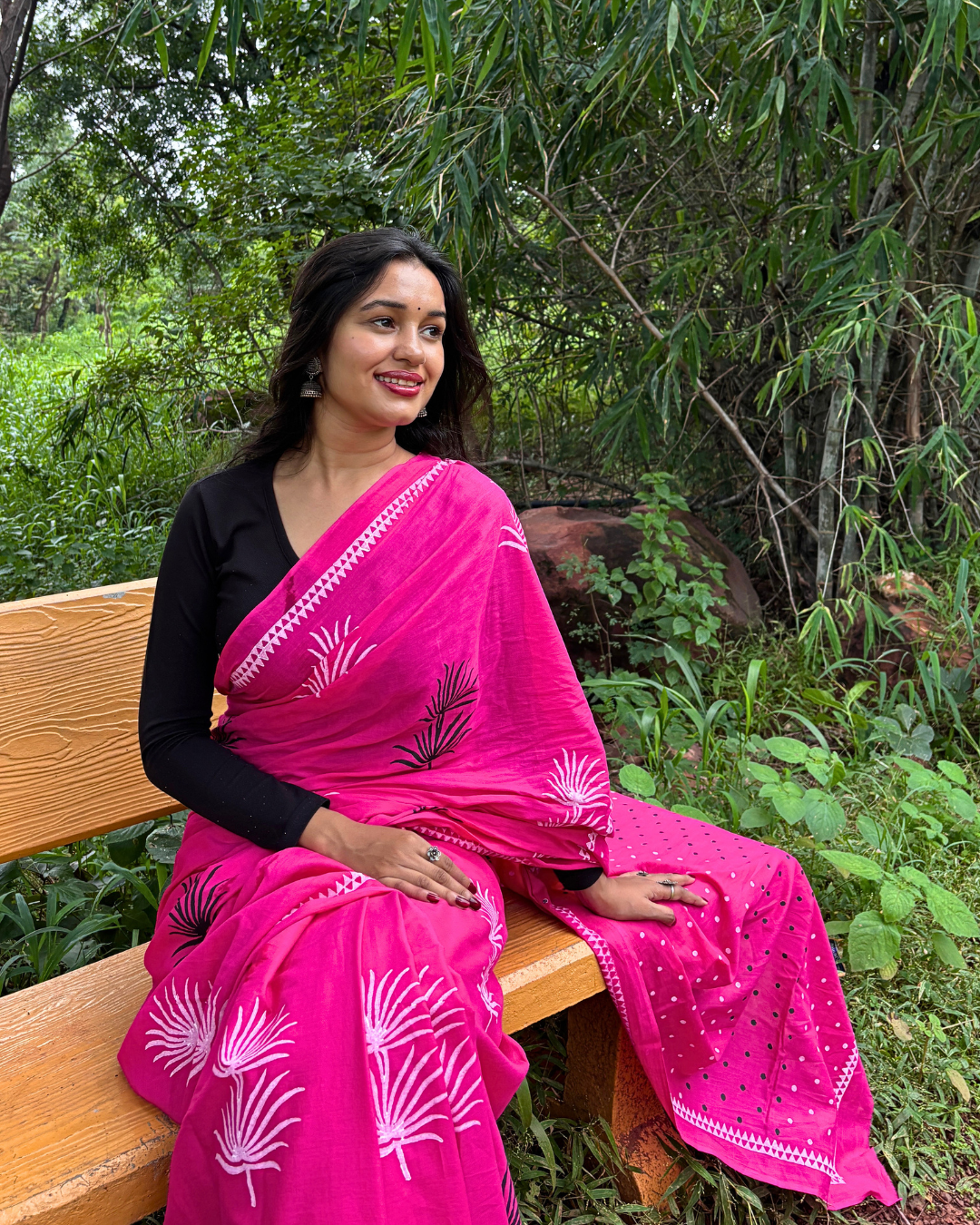 Pink Saree Portrait in Nature Woman in vibrant pink saree sitting on a wooden bench surrounded by greenery